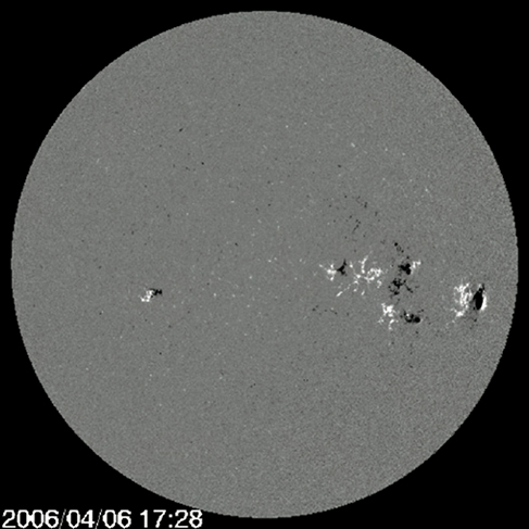 A magnetogram of the sun, which appears as a gray disc against a black background, with white and black spots scattered on it. Most of the spots are concentrated in the center right part of the image.